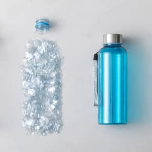 A drink bottle in vibrant blue with a stainless steel lid and a carrying strap, alongside recycled plastic pieces.