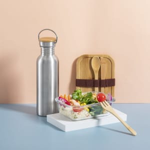 A drink bottle in silver metal with a wooden lid, accompanied by a salad bowl and bamboo utensils.