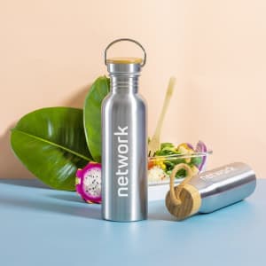 A drink bottle with a stainless steel body, bamboo lid, and a branding logo, set against a pastel background.