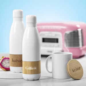A drink bottle in white with a bamboo accent and branding, alongside a steaming mug and a retro pink radio.