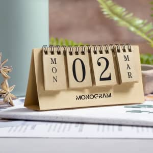 A desk calendar with a tan base, featuring black numbered and day tabs, and a logo at the bottom.