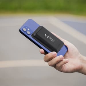 A black Vekmar Power Bank is being held against a blue smartphone, showcasing its compact design.