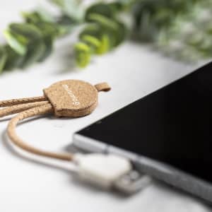 A tan charging cable with a textured design, connected to a smartphone, set against a blurred green background.