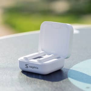 A pair of white earbuds in an open charging case on a table, featuring a branding logo.
