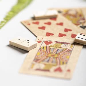 A selection of playing cards and dominoes in cream and red, with a leafy backdrop, arranged on a light surface.