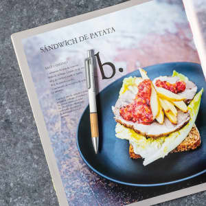 A metal pen with a silver barrel and wooden accents, placed on an open magazine featuring a food recipe.