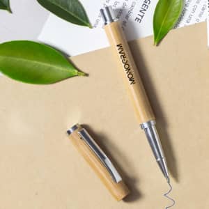 A bamboo roller pen with a silver tip and clip, surrounded by green leaves and paper.