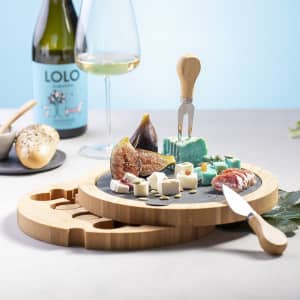 A bamboo cheese board set featuring a slicer, knife, and an assortment of cheese, figs, and cold cuts.