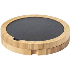 A cheese board set featuring a circular bamboo base and a black slate surface. It includes a branding logo.