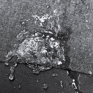 A close-up of water droplets beading on a textured, dark grey fabric surface, demonstrating waterproof properties.