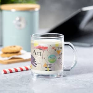 A clear glass mug featuring a colourful design with artistic elements, accompanied by a striped straw and cookies.