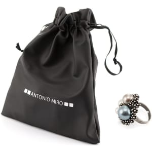 An adjustable ring with a cluster of pearls in grey, white, and blue beside a black drawstring pouch.