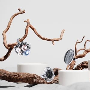 A collection of adjustable rings featuring pearls and a black stone, displayed on textured surfaces with natural branches.