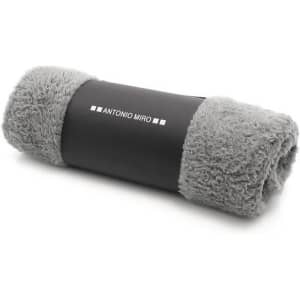 A rolled-up grey blanket with soft, fluffy texture and a black band featuring a logo.