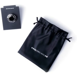 A black adjustable ring with a decorative design, accompanied by a black drawstring pouch and branded card.
