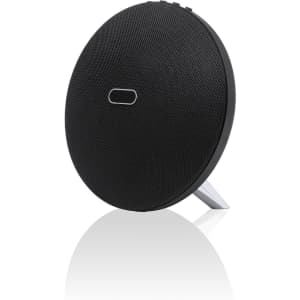 A round black speaker with a textured surface and a built-in stand, featuring a simple logo on the front.