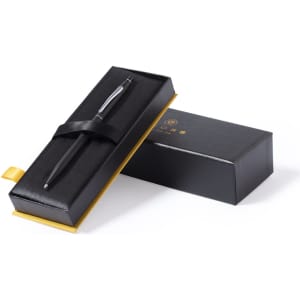 A black metal pen resting in a sleek black and gold presentation box with a ribbon. The box features a logo.