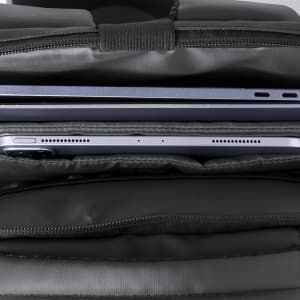 A black backpack with compartments containing a laptop and a tablet. The zippers are visible along the side.