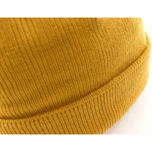 A mustard-yellow beanie with a ribbed texture and folded brim, featuring a logo on the side.