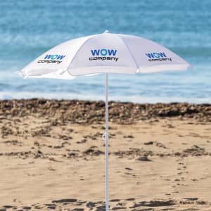 A white beach umbrella with a logo, set against a sandy beach and ocean backdrop.