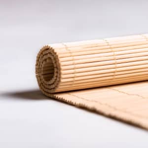 A rolled bamboo place mat in a natural finish, featuring a simple woven design. It has a branding logo.