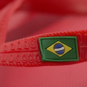 A pair of red flip flops featuring a logo with the Brazilian flag on the strap.