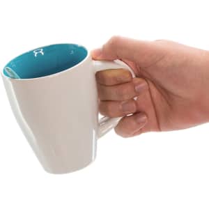 A coffee mug with a white exterior and a teal interior, held in a hand. It features a logo on the surface.