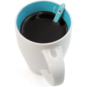 A coffee mug in white with a turquoise interior, filled with black coffee and featuring a small spoon.