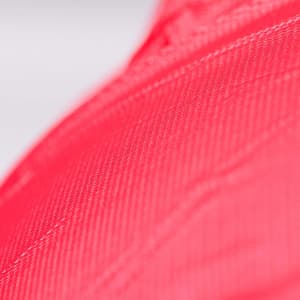 A close-up view of textured fabric in bright red colour, featuring a subtle sheen. The item has a logo.