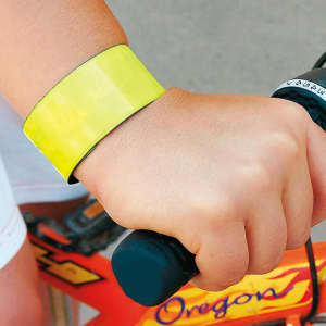 A reflective bracelet in bright yellow is worn on a wrist, gripping a bicycle handlebar. The image features a logo on the handle.