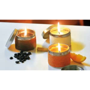 Three aromatic candles in containers with metal lids, featuring orange, brown, and cream colours, surrounded by coffee beans and an orange slice.