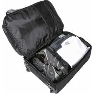 A black wheeled travel bag, open to reveal shoes, a shirt, and jeans neatly packed inside.