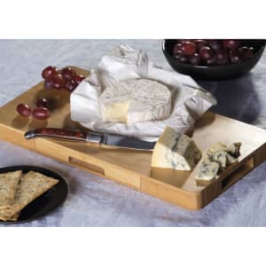 A cheese board set featuring a wooden board, a knife, various cheeses, crackers, grapes, and a bowl of grapes.