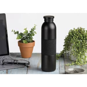 A drink bottle in matte black with a textured black band, placed on a wooden surface alongside plants and office items.