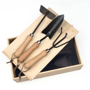 A wooden garden box containing three black-handled gardening tools with wooden grips.