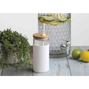 A drink bottle with a white body and bamboo lid, positioned next to a glass dispenser with citrus fruits and greenery.