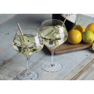 Two elegant glass goblets filled with a clear drink, garnished with cucumber slices and peppercorns, on a rustic wooden surface.