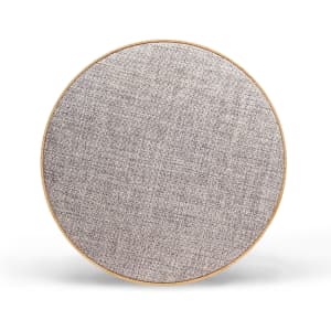 A round Bluetooth speaker in a light grey fabric finish with a wooden border. It features a logo.