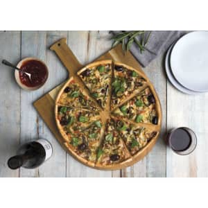 A wooden pizza peel featuring a pizza sliced into pieces, garnished with greens, served with dipping sauce and wine.