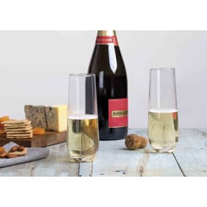 A bottle of champagne with two clear stemless flutes, set on a rustic table with cheese and snacks.