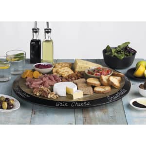 A round wooden serving platter features various cheeses, meats, nuts, and breads, with bowls of olives and salad.