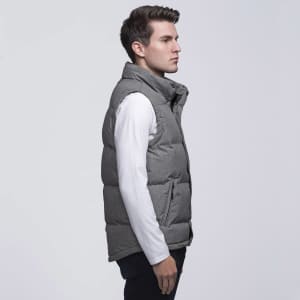 A man models a grey puffer vest with a high collar, worn over a long-sleeve white shirt. The vest has a logo.