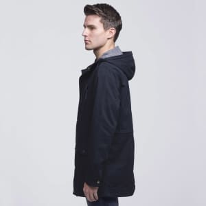 A twill jacket in navy blue featuring a hood, side pockets, and a grey inner lining. It has a logo on the front.