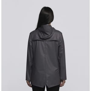 A woman stands facing away, wearing a grey rain jacket with a hood. The jacket has a simple design and includes a logo.
