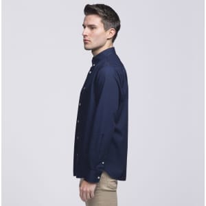 A navy blue button-up shirt with a collar, displayed on a model facing sideways. The shirt has a logo.