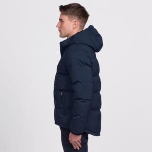 A man wearing a navy blue puffer jacket with a hood, featuring a zippered pocket on the side.