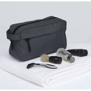 A dark grey toiletry bag with grooming items including a razor, shaving brush, and travel-sized bottles, placed on a white towel.