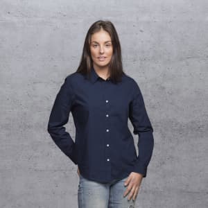 A woman wearing a navy blue button-up shirt, with long sleeves and a collar, standing against a grey background.