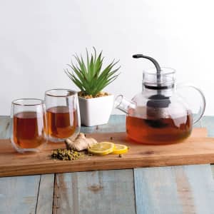 A tea set featuring a glass teapot, two glasses, lemon slices, ginger, and a small potted plant on a wooden tray.