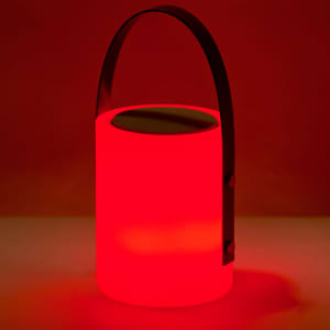 A red speaker lamp with a cylindrical body and a handle, featuring a speaker on top and a smooth finish.